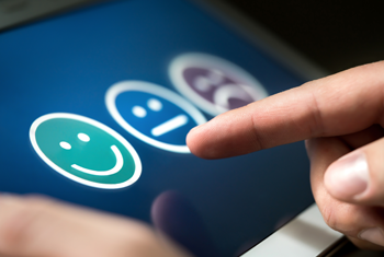 Finger selecting a happy face icon on a screen to indicate satisfaction. A neutral and sad face icons are visible.